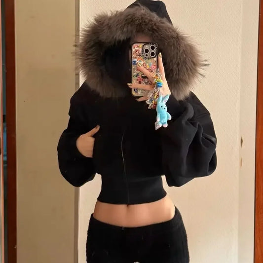 Person wearing a black hoodie with a fur-lined hood, taking a mirror selfie.
