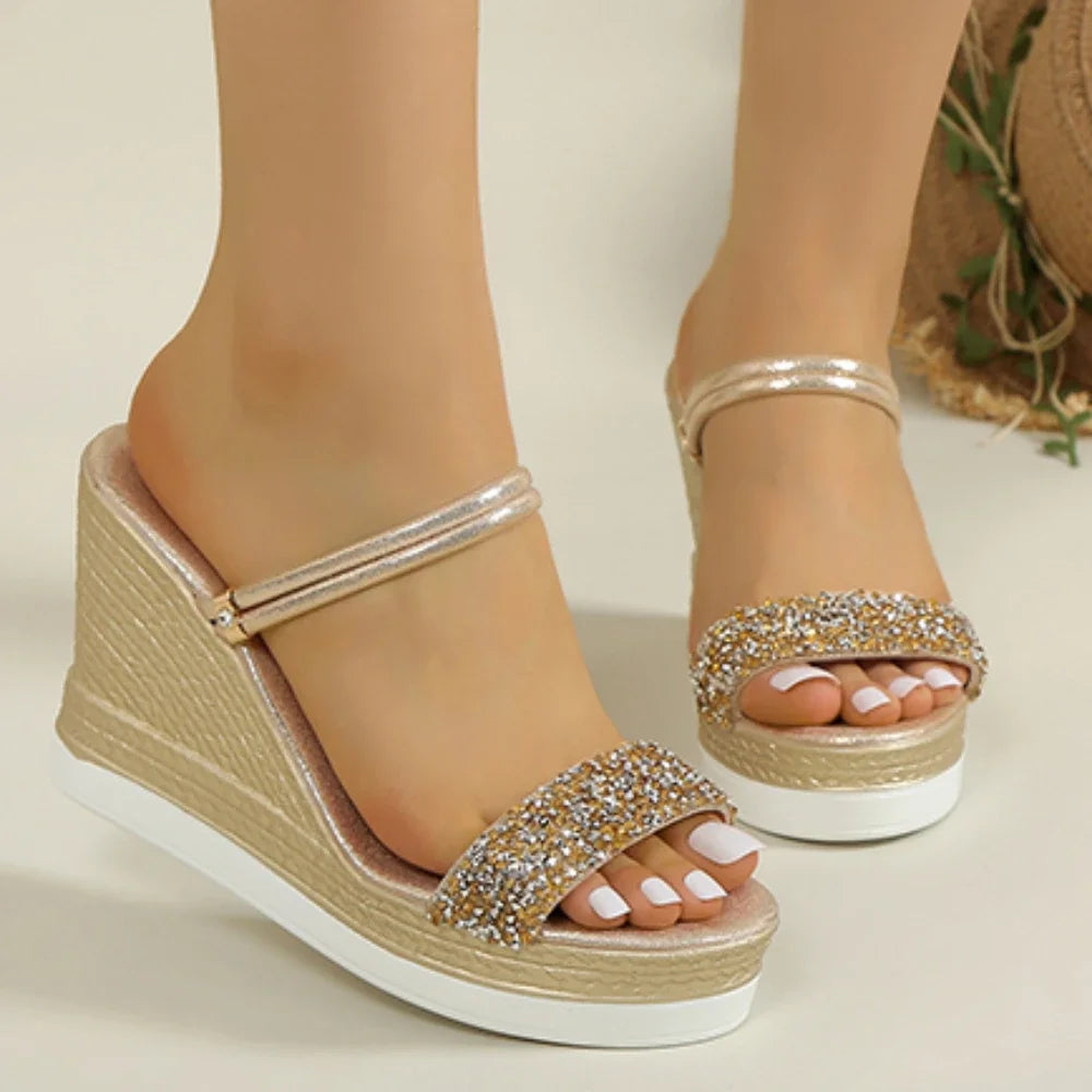 Gold wedge sandals with rhinestone straps worn by a person on a neutral background