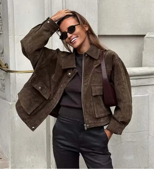 Woman wearing a brown suede jacket and sunglasses, standing on stone steps.