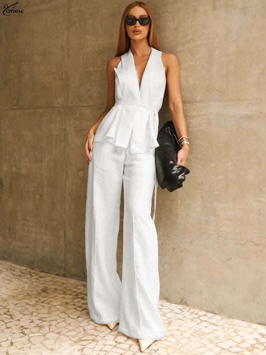 Woman wearing a white sleeveless jumpsuit against a beige wall.