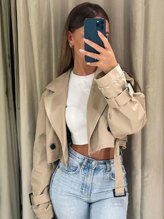 Person wearing a beige trench coat over a white top and blue jeans, taking a mirror selfie.