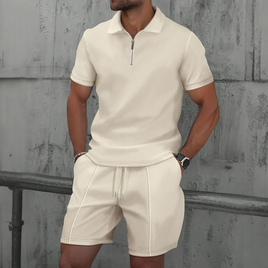 Man wearing a beige polo shirt and shorts set against a textured wall.