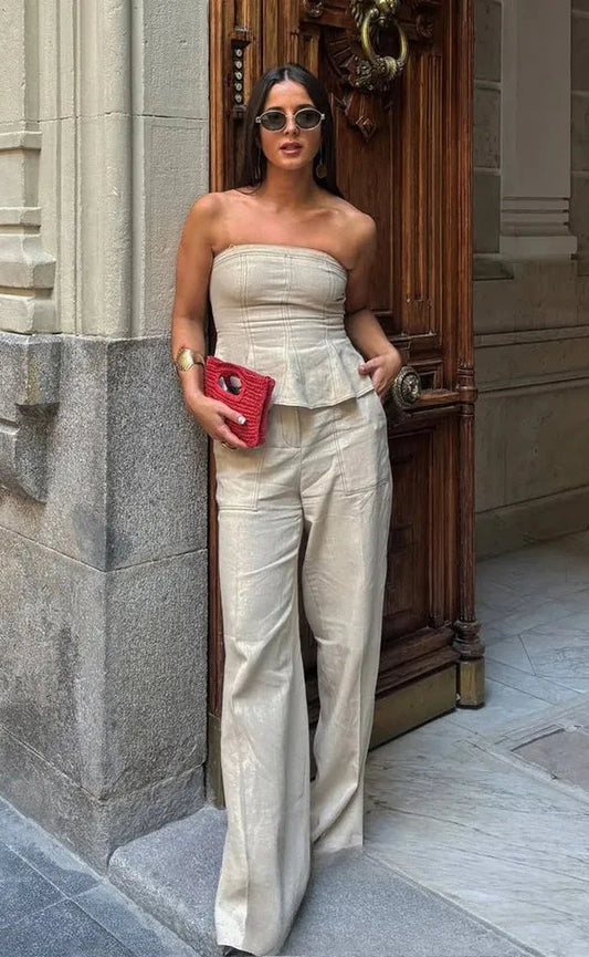 Woman in a strapless top and wide-leg pants standing in front of a stone building entrance.