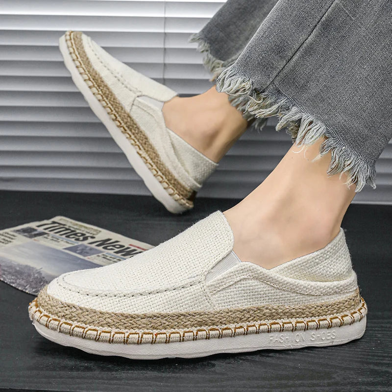 White loafers with jute trim worn by a person on a dark surface.