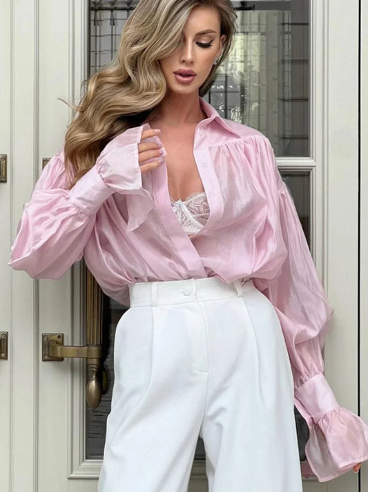 Woman wearing a pink blouse with ruffled sleeves and white pants standing in front of a door.