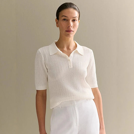 Woman wearing a white knit top and white pants against a beige background