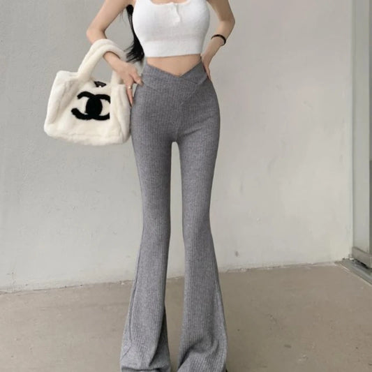 Person wearing gray flared pants and a white top, holding a Chanel handbag against a plain background.