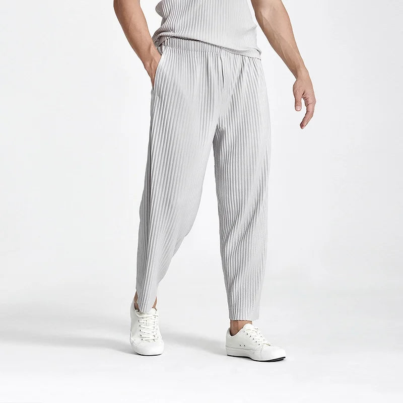 Person wearing light gray pleated pants and white sneakers on a white background