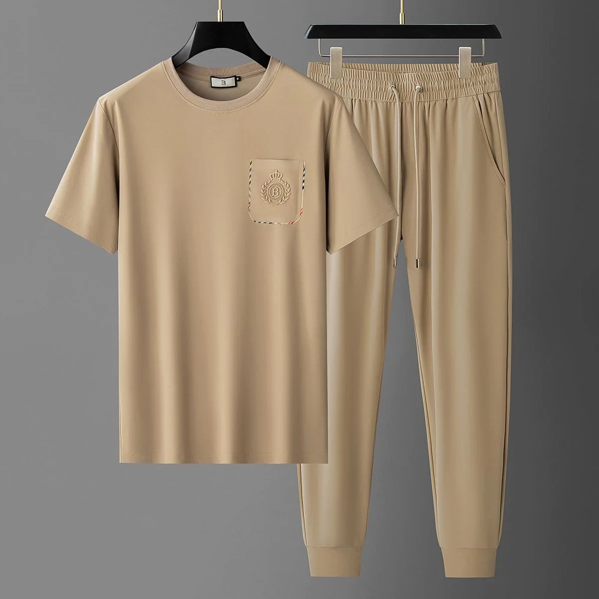 Beige t-shirt and pants set on hangers against a gray background