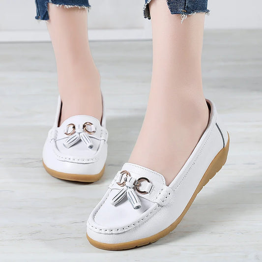 White loafers with decorative elements worn by a person on a light wooden floor.