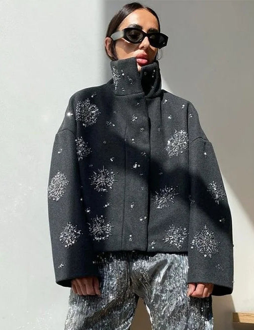 Person wearing a dark gray coat with snowflake patterns and matching pants, standing against a light-colored wall.