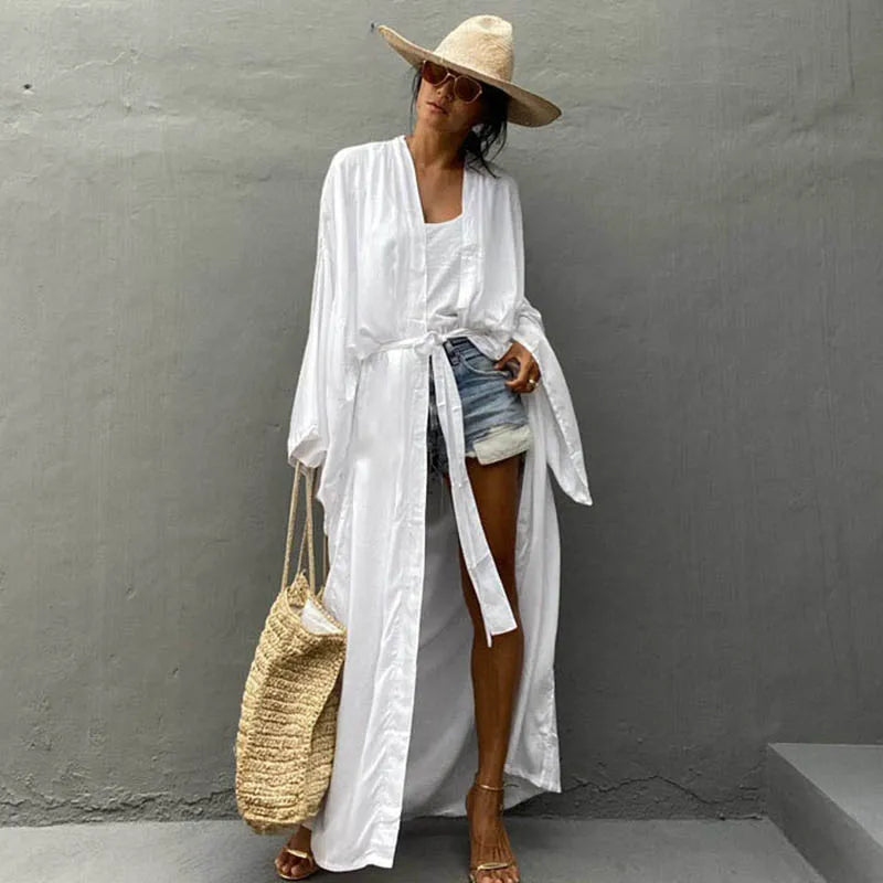 Woman wearing a white robe and straw hat against a gray wall