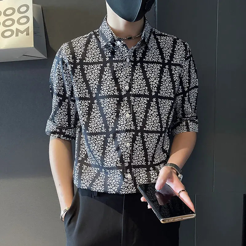 Person wearing a patterned shirt holding a phone against a dark background