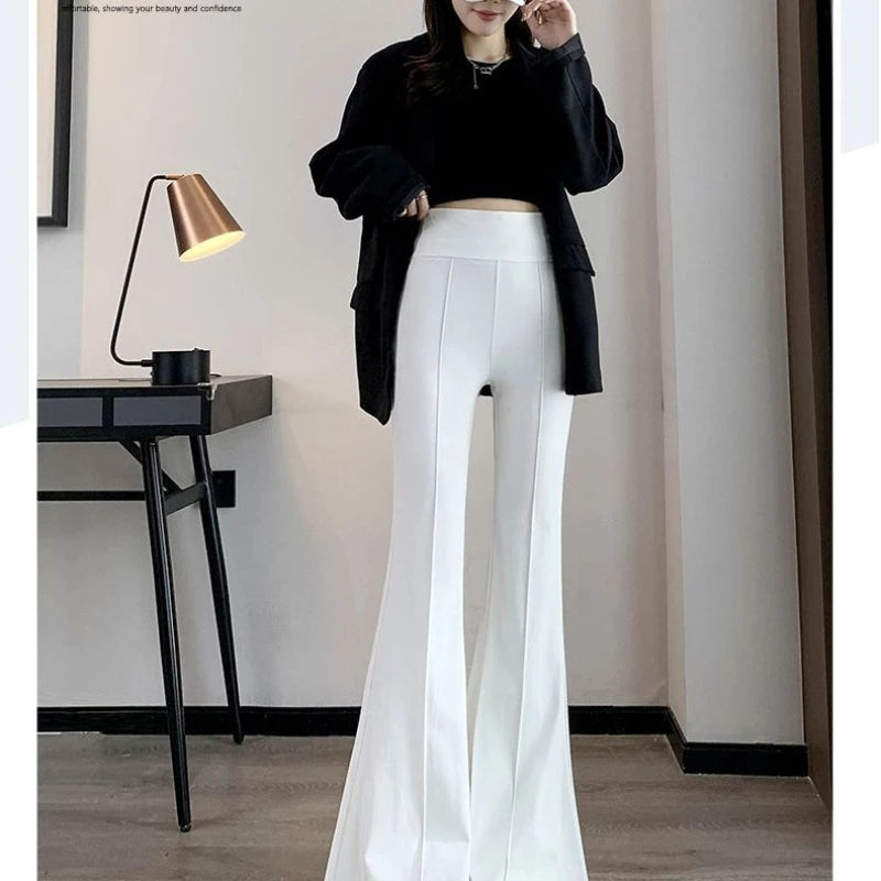 Person wearing a black top and white pants in a room with a lamp and desk.