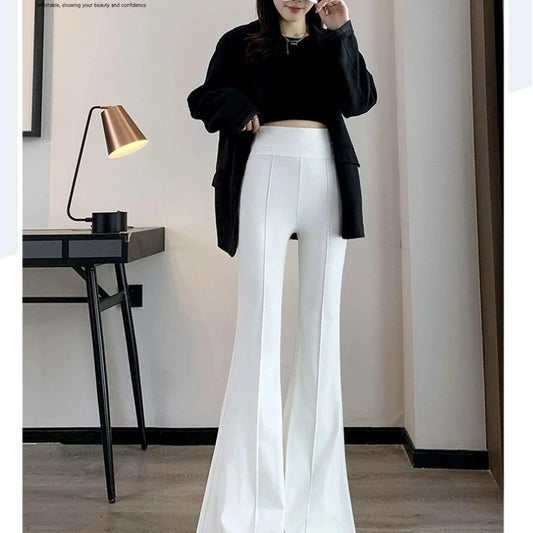 Person wearing a black top and white pants in a room with a lamp and desk.