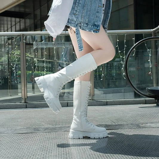 Person wearing white knee-high boots on a city street.