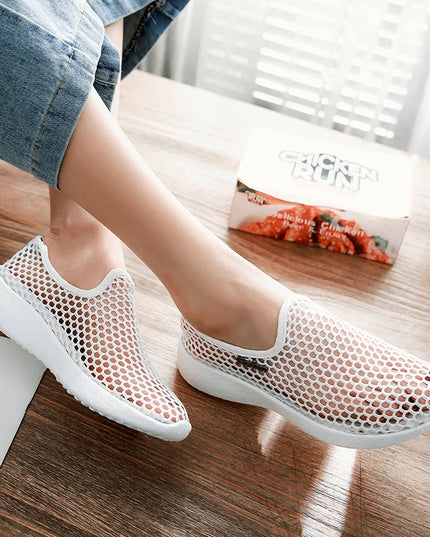 White mesh shoes worn by a person on a wooden floor.