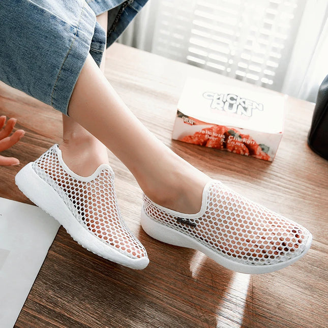 White mesh shoes worn by a person on a wooden floor.