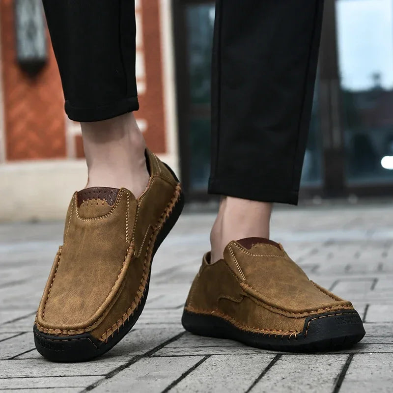 Brown loafers worn with black pants on a blurred outdoor background