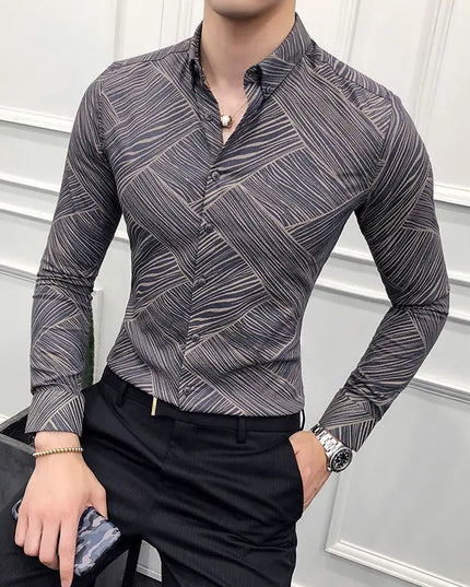 Man wearing a patterned gray shirt and black pants against a white wall.