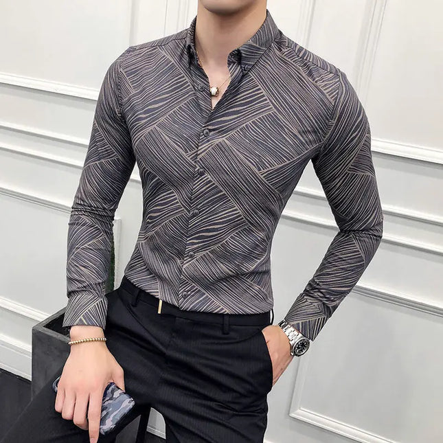 Man wearing a patterned gray shirt and black pants against a white wall.