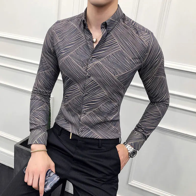 Man wearing a patterned gray shirt and black pants against a white wall.