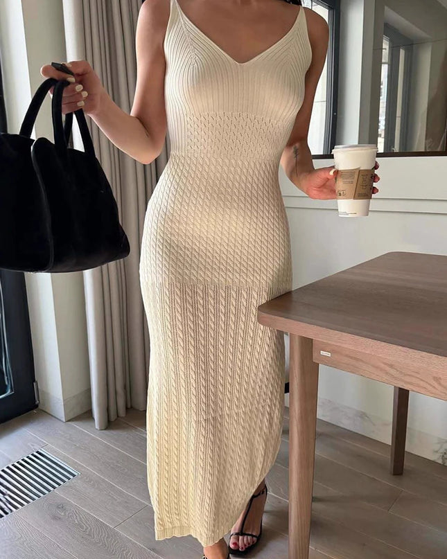 Woman in a beige knit dress holding a black handbag and a coffee cup indoors.