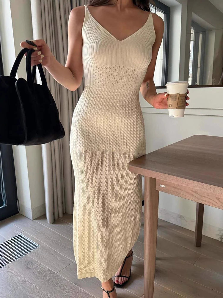 Woman in a beige knit dress holding a black handbag and a coffee cup indoors.