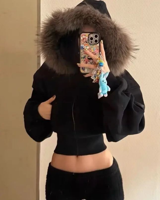 Person wearing a black hoodie with a fur-lined hood, taking a mirror selfie.