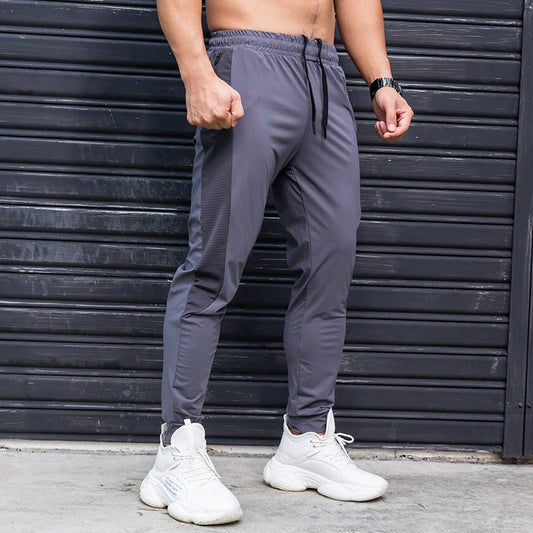 Person wearing gray jogger pants and white sneakers in front of a black metal shutter.