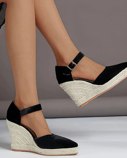 Black wedge sandals with espadrille sole worn by a person on a gray background