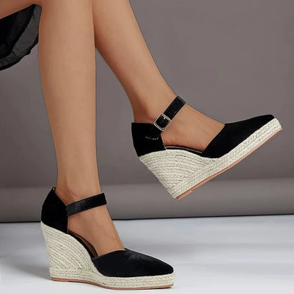 Black wedge sandals with espadrille sole worn by a person on a gray background