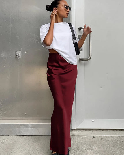 Woman wearing a white top and maroon pants standing against a gray wall.