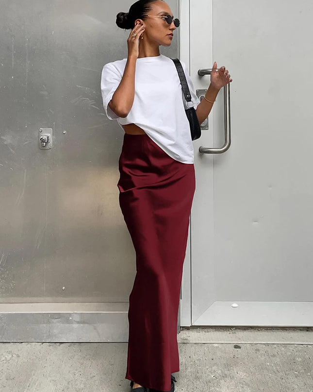 Woman wearing a white top and maroon pants standing against a gray wall.
