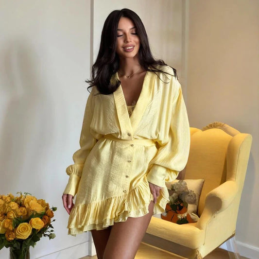 Woman in a yellow outfit sitting on a yellow chair with a white wall and floral arrangement in the background