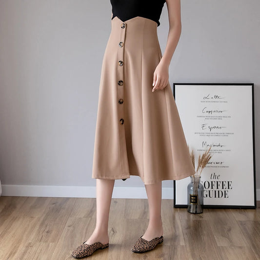 Person wearing a beige button-up skirt in a room with a framed poster on the wall.