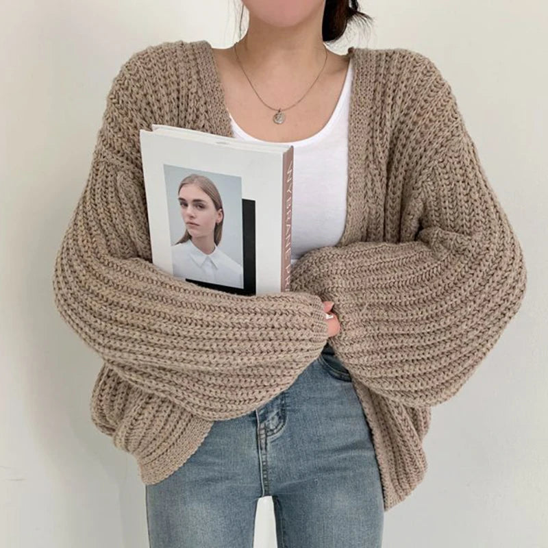 Person wearing a chunky knit beige sweater holding a photo album with a white cover.
