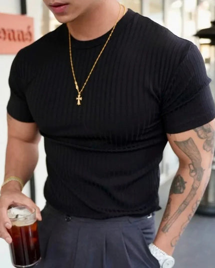 Person wearing a black t-shirt and gold necklace, holding a drink in an indoor setting.