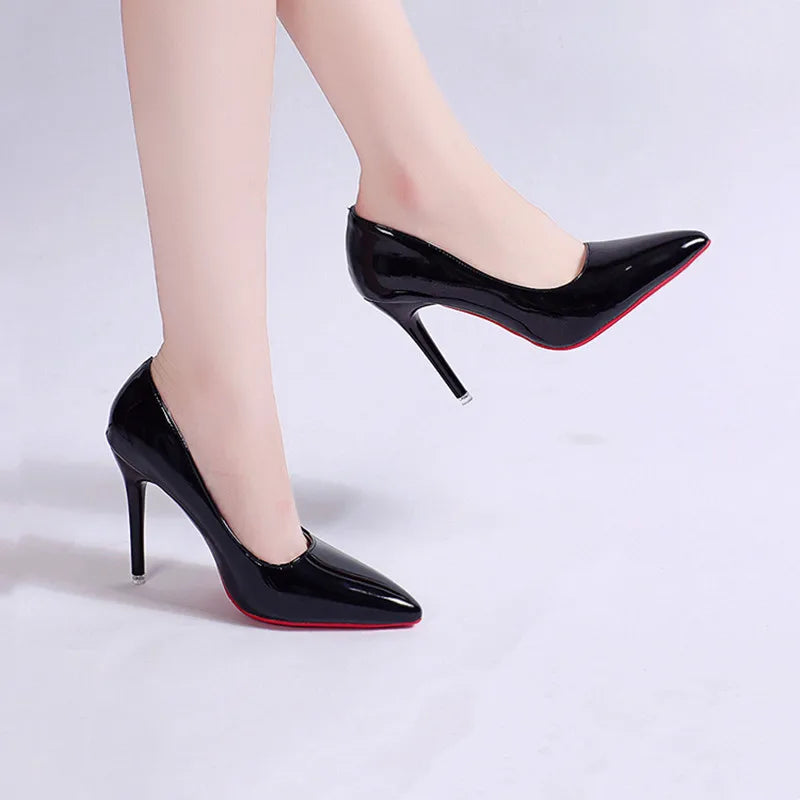 Black high-heeled shoes with red soles worn by a person on a light gray background
