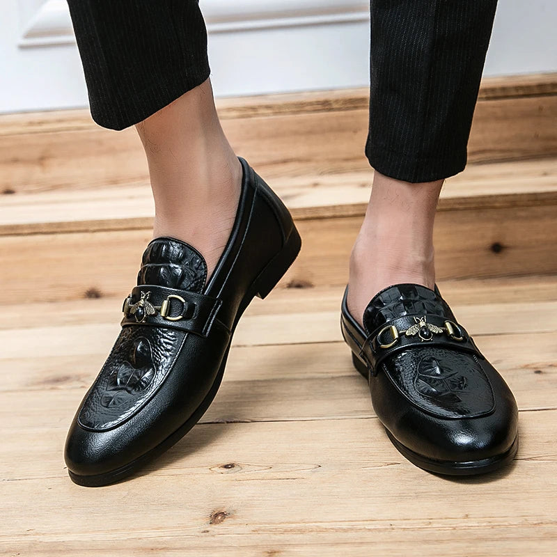 Black leather shoes with gold buckles worn by a person on a wooden floor.