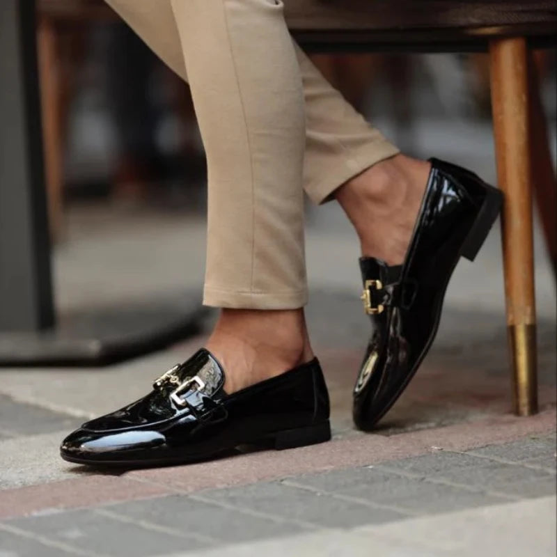 Black patent leather loafers worn with beige pants on a blurred background
