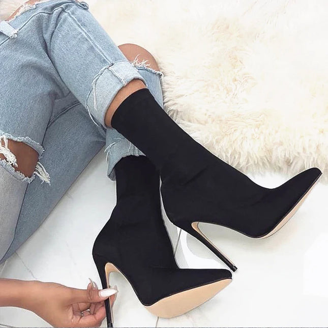 Black knee-high boots being worn with light blue jeans on a white surface.