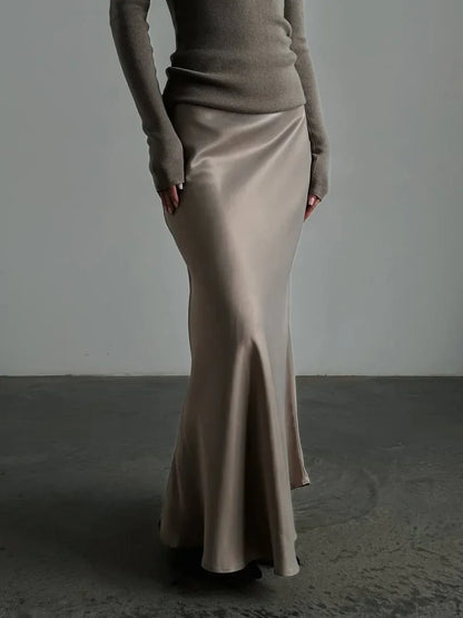 Person wearing a beige long skirt and brown top against a plain background