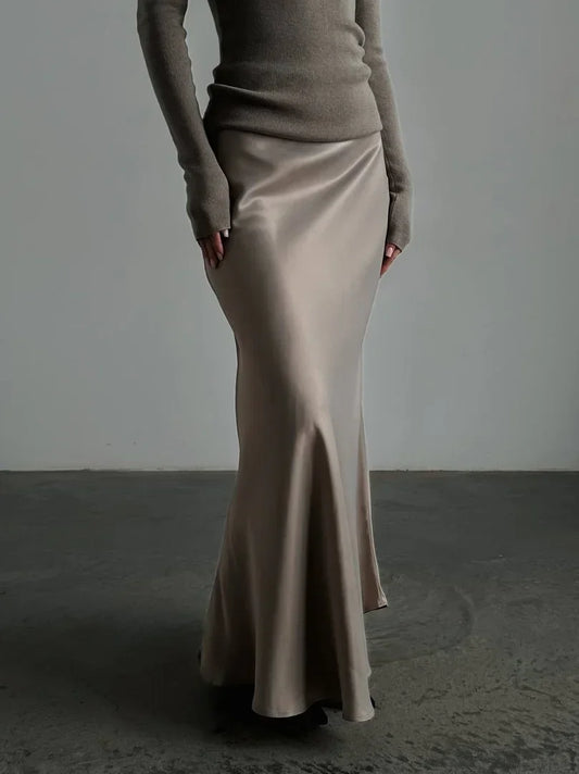 Person wearing a beige long skirt and brown top against a plain background