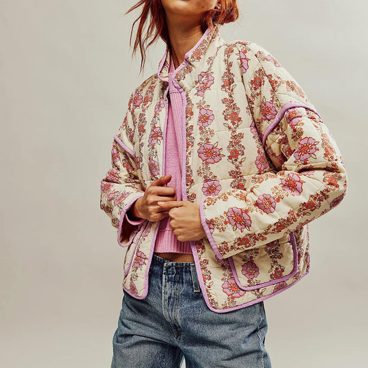 Person wearing a floral quilted jacket over a pink shirt and blue jeans on a plain background