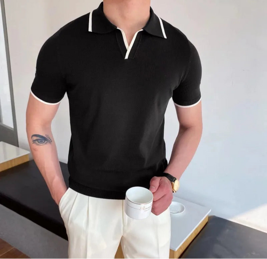 Person wearing a black polo shirt with white trim, holding a white cup indoors.