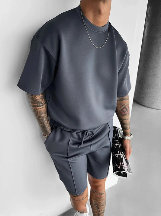 Person wearing a gray outfit with tattoos visible, holding a black and white bag.