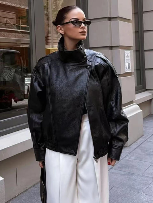 Person wearing a black leather jacket and sunglasses on a city street.