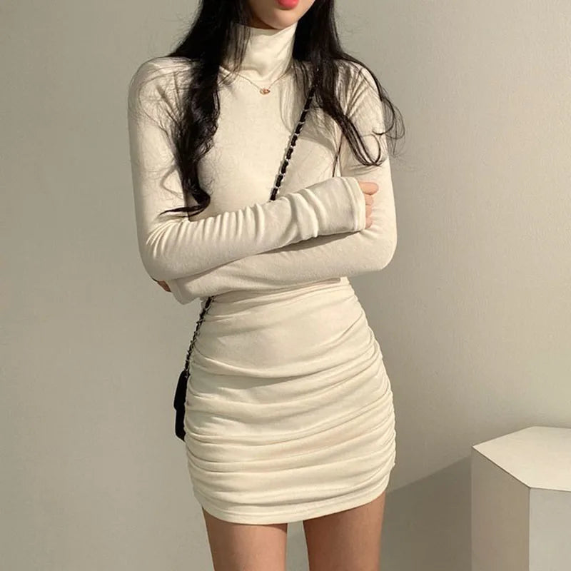 Woman wearing a beige long-sleeve dress against a plain background