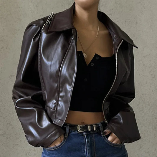 Person wearing a brown leather jacket over a black top with a neutral background